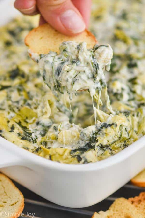 a bagel chip dipping into spinach and artichoke dip