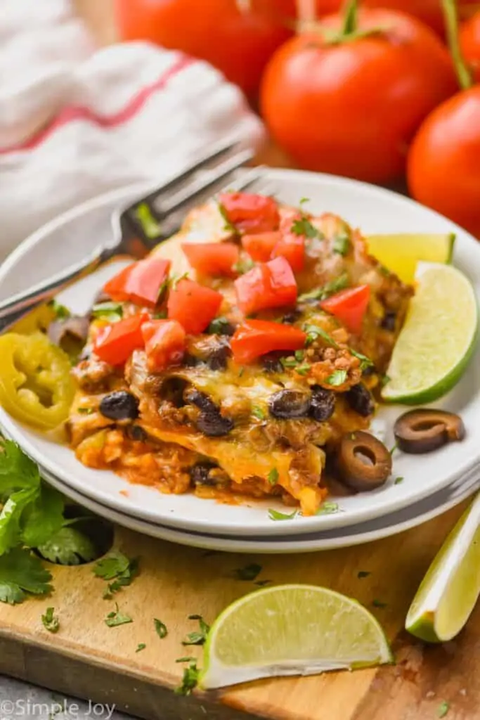 enchilada casserole recipe cut (like a lasagna) on a plate and topped with fresh tomatoes and olive slices