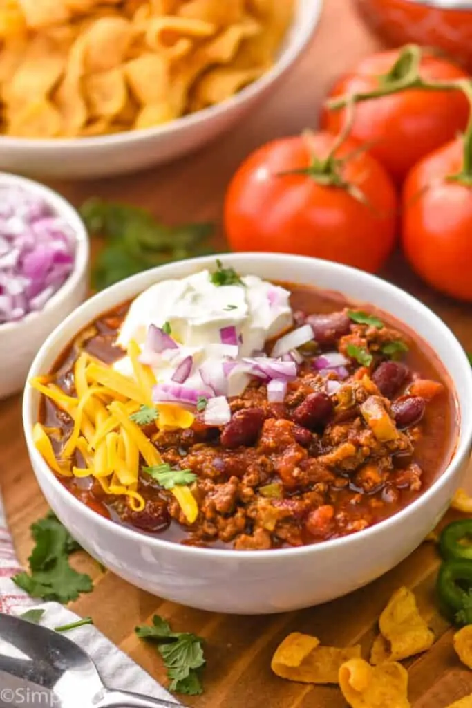 small white bowl full of homemade chili made in the crockpot, topped with sour cream, shredded cheese, diced onions, and fresh cilantro