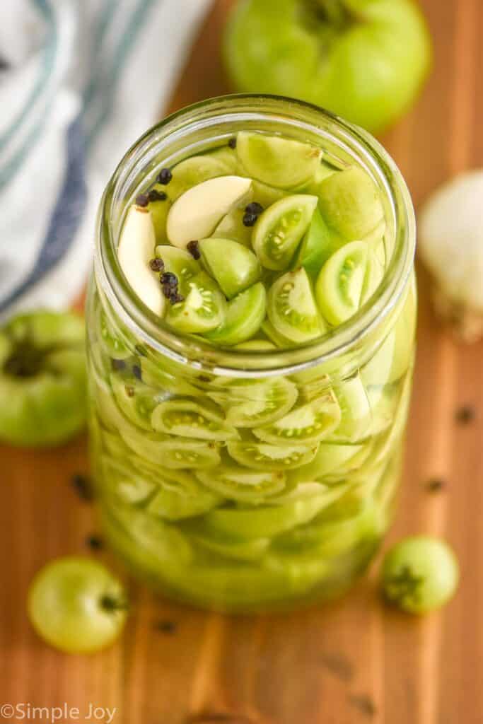 overhead view of a jar of pickled green tomatoes with peppercorns and garlic cloves