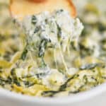 a bagel chip dipping into spinach and artichoke dip - 13