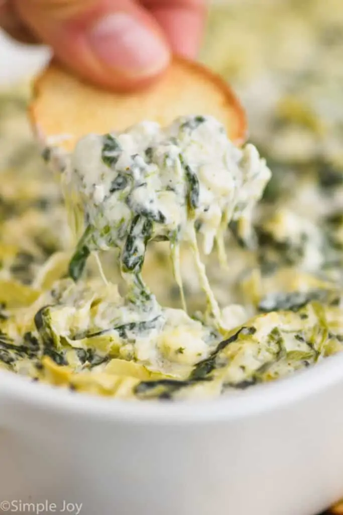 a bagel chip dipping into spinach and artichoke dip