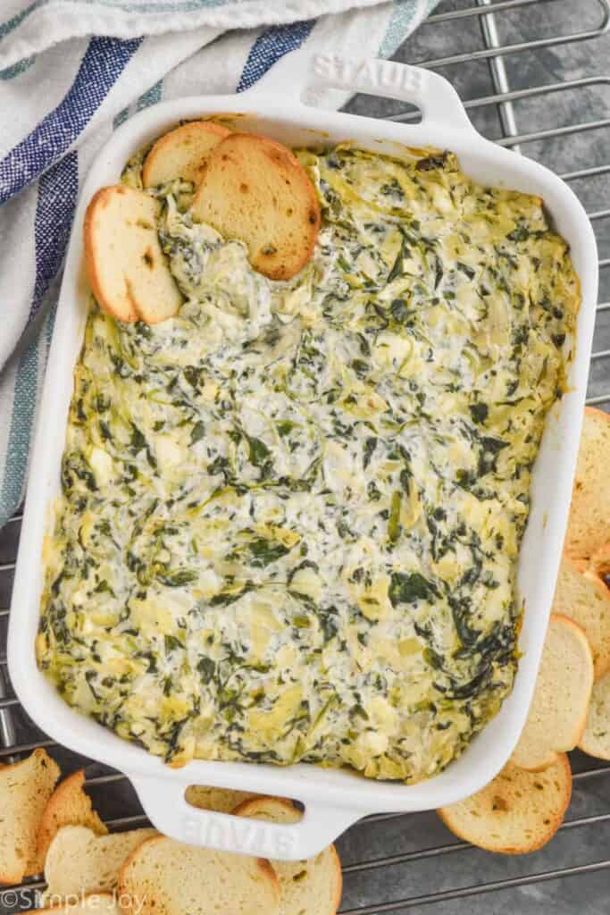 overhehead view of baked spinach artichoke dip in a white casserole dish surrounded by bagel chips