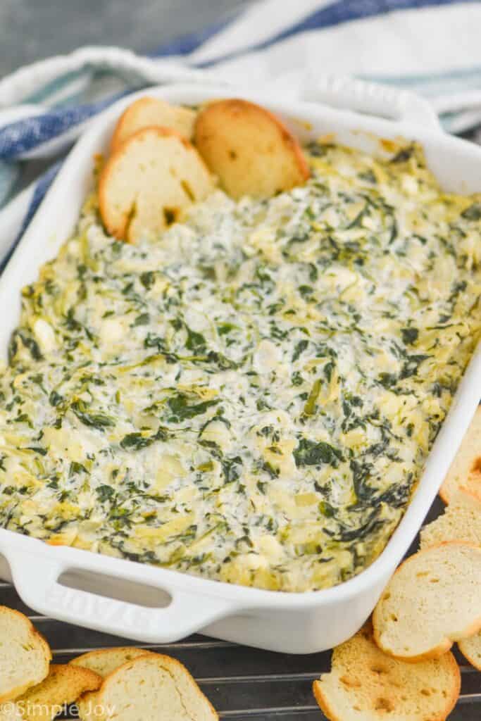 small white casserole dish full of spinach artichoke dip recipe surrounded by bagel chips