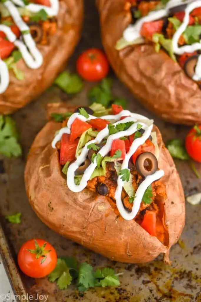 close look at a whole sweet potato that has been topped with taco meat, olives, sour cream, cilantro, and diced tomatoes