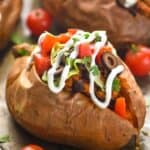 close up of a taco stuffed sweet potato on a baking sheet that has been topped with sour cream, cilantro, sliced olives, diced tomatoes, and lettuce - 6