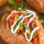 close look at a whole sweet potato that has been topped with taco meat, olives, sour cream, cilantro, and diced tomatoes