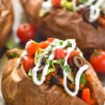 close up of a taco stuffed sweet potato on a baking sheet that has been topped with sour cream, cilantro, sliced olives, diced tomatoes, and lettuce