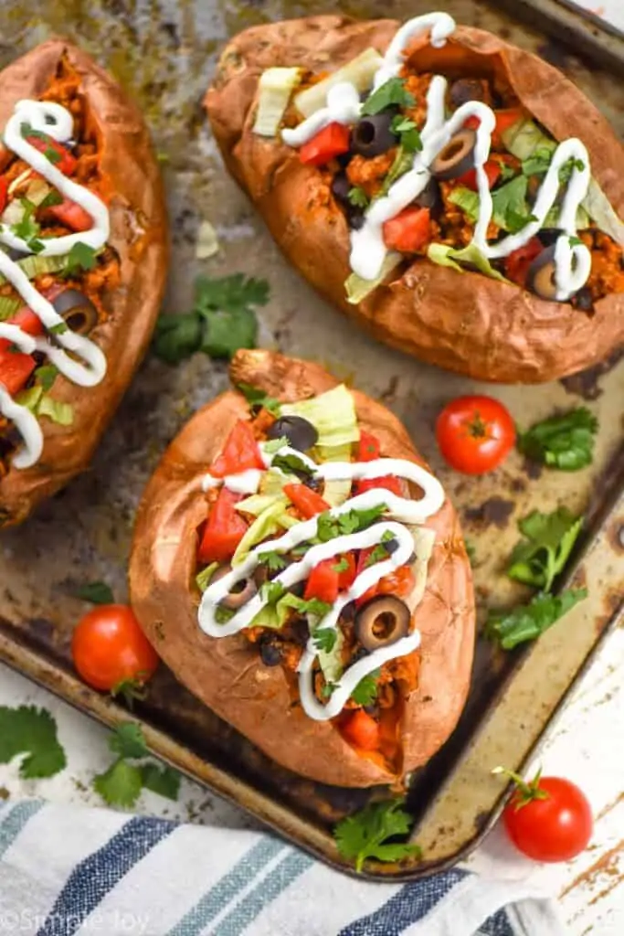 overhead view of taco stuffed sweet potato recipe on a baking sheet topped with sour cream, cilantro, tomatoes, and lettuce