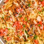 overhead close up view of cajun chicken Alfredo with sliced chicken on top of fettucine garnished with fresh tomatoes, parsley, and parmesan