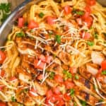 overhead close up view of cajun chicken Alfredo with sliced chicken on top of fettucine garnished with fresh tomatoes, parsley, and parmesan