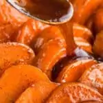 syrupy mixture being poured over casserole dish with candied sweet potatoes