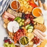 an overhead view of a charcuterie board with cheeses, meats, crackers, vegetables, fruits, and nuts