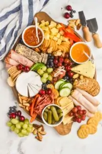 an overhead view of a charcuterie board with cheeses, meats, crackers, vegetables, fruits, and nuts