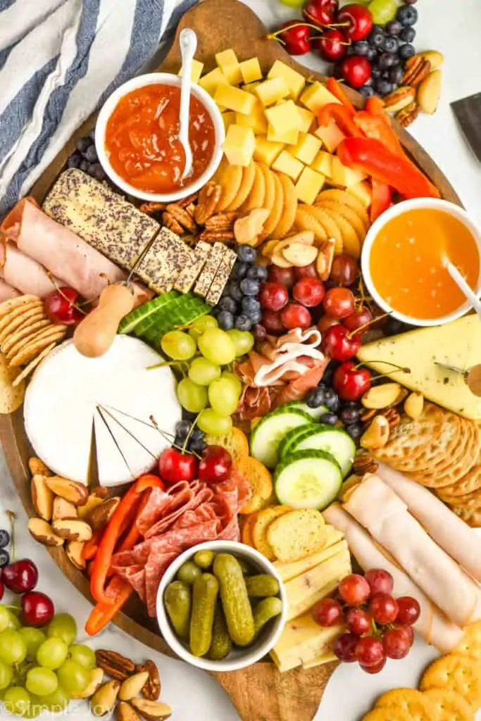 an overhead view of a charcuterie board with cheeses, meats, crackers, vegetables, fruits, and nuts