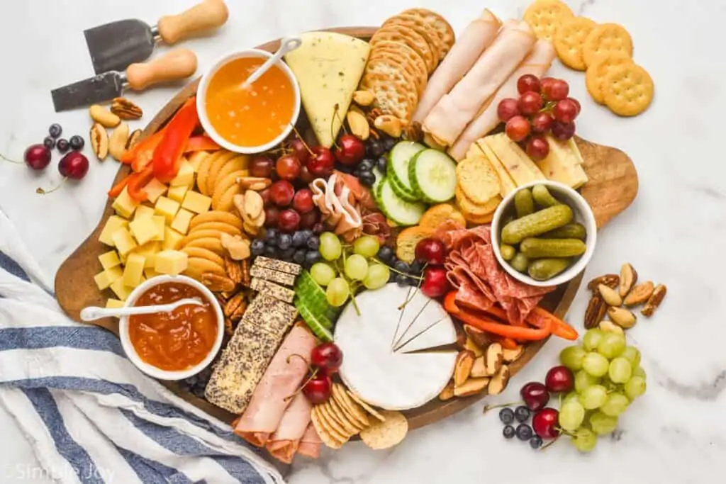 an overhead view of a charcuterie board with cheeses, meats, crackers, vegetables, fruits, and nuts