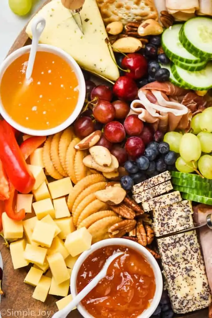 a close up of a charcuterie board with cheeses, dips, crackers, berries, and vegetables