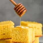 honey wand dripping honey over two pieces of stacked cornbread