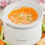 a small crockpot with buffalo chicken dip in it, garnished with blue cheese and sliced green onions