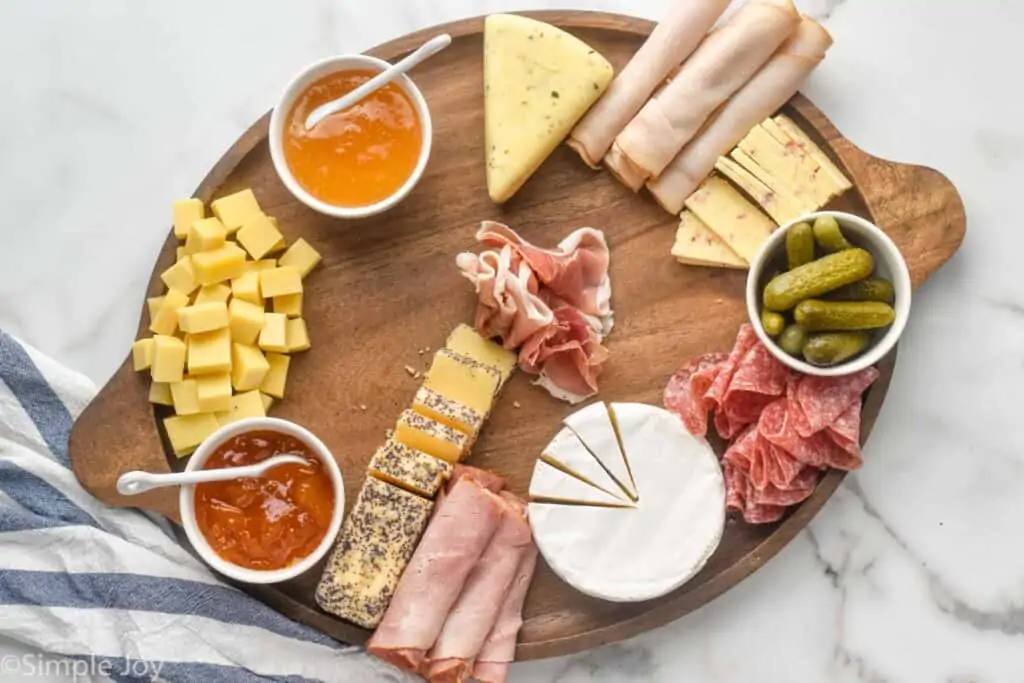 a large wooden tray with bowls for condiments, deli meats, and cheeses