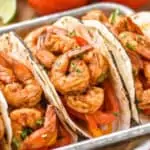 three shrimp fajitas on a metal tray garnished with fresh cilantro