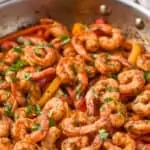 a frying pan full of shrimp fajita recipe topped with fresh cilantro and two lime wedges