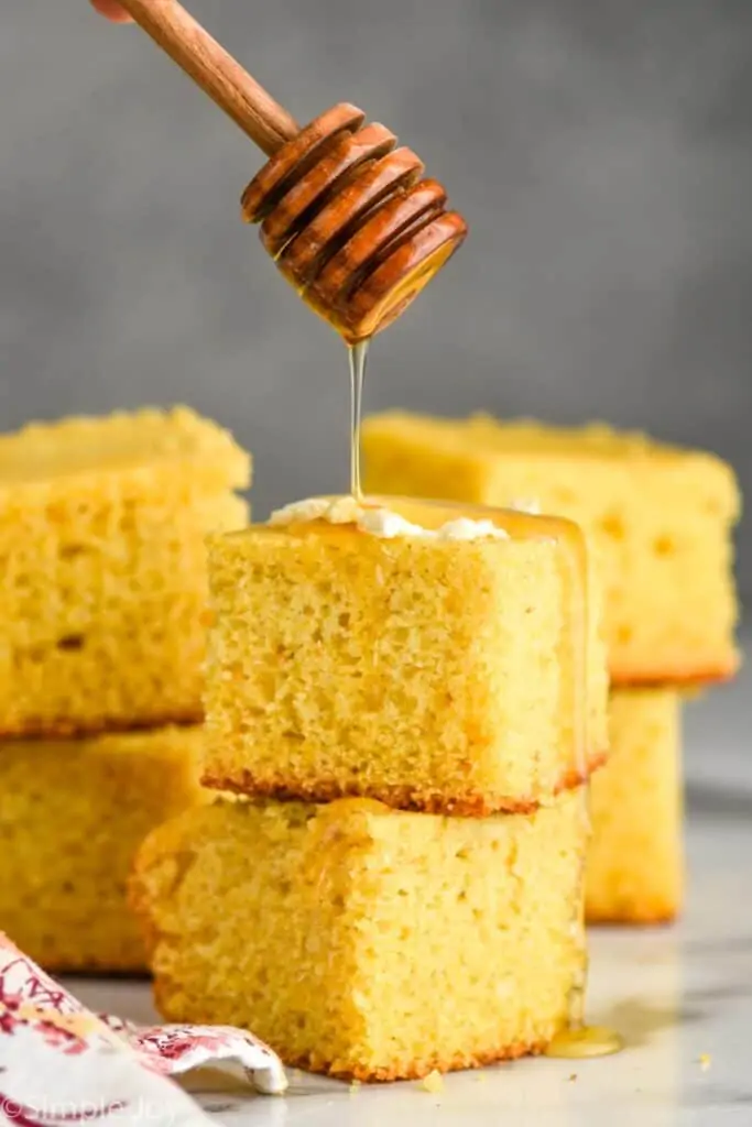 honey wand dripping honey over two pieces of stacked cornbread