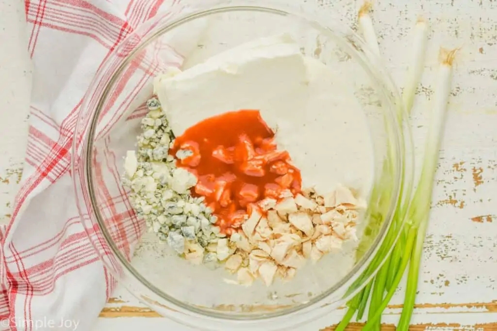 overhead of a clear bowl full of buffalo chicken dip ingredients