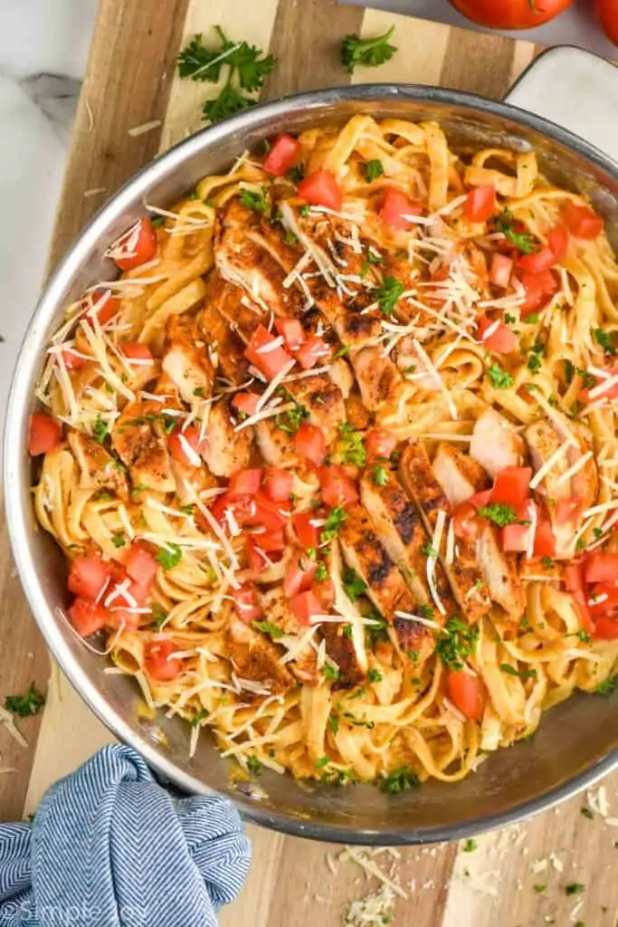 overhead close up view of cajun chicken Alfredo with sliced chicken on top of fettucine garnished with fresh tomatoes, parsley, and parmesan