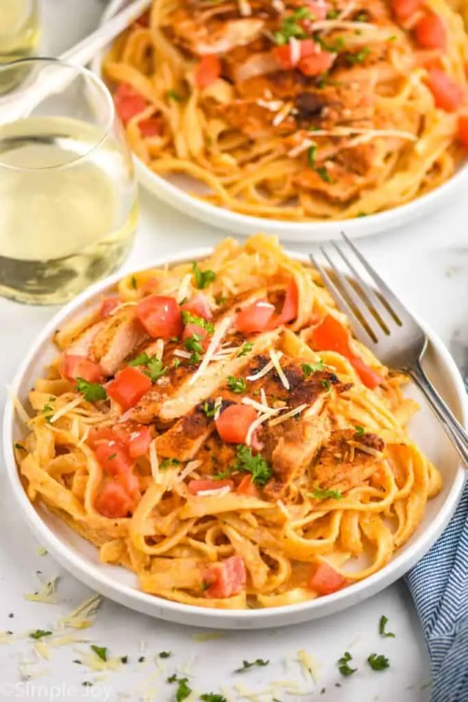 small white plate with cajun chicken Alfredo, garnished with fresh tomatoes, parsley, and shredded parmesan