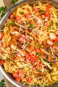 overhead close up view of cajun chicken Alfredo with sliced chicken on top of fettucine garnished with fresh tomatoes, parsley, and parmesan