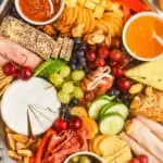 an overhead view of a charcuterie board with cheeses, meats, crackers, vegetables, fruits, and nuts