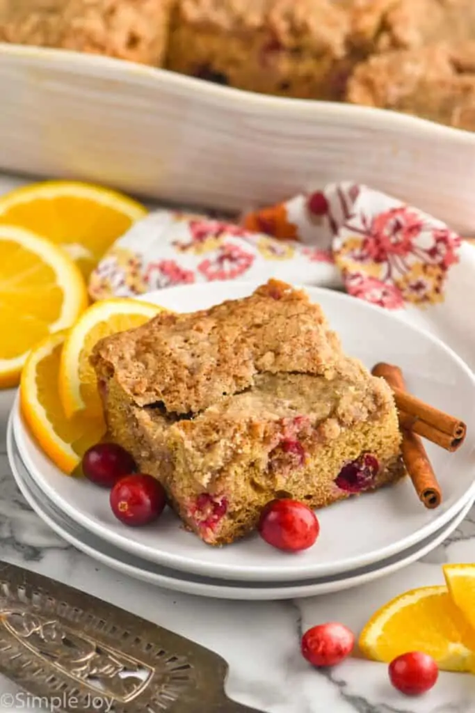 a piece of coffee cake recipe on a plate with cinnamon sticks, cranberries, and orange slices