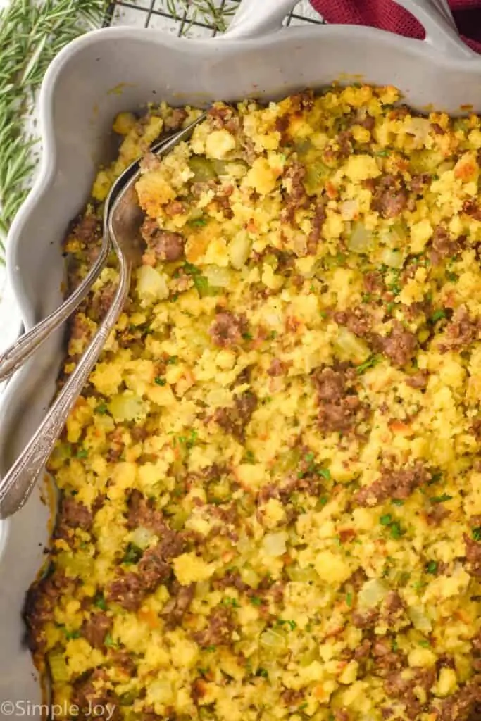 overhead view of a baking dish with cornbread stuffing recipe with two utensils sticking put