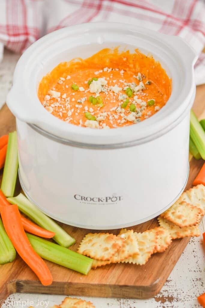 a small crockpot with buffalo chicken dip in it, garnished with blue cheese and sliced green onions