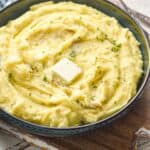 side view of a bowl of creamy mashed potatoes with a pad of melting butter, parsley, and black pepper - 5