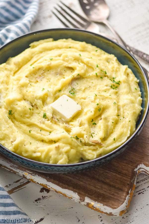 side view of a bowl of creamy mashed potatoes with a pad of melting butter, parsley, and black pepper