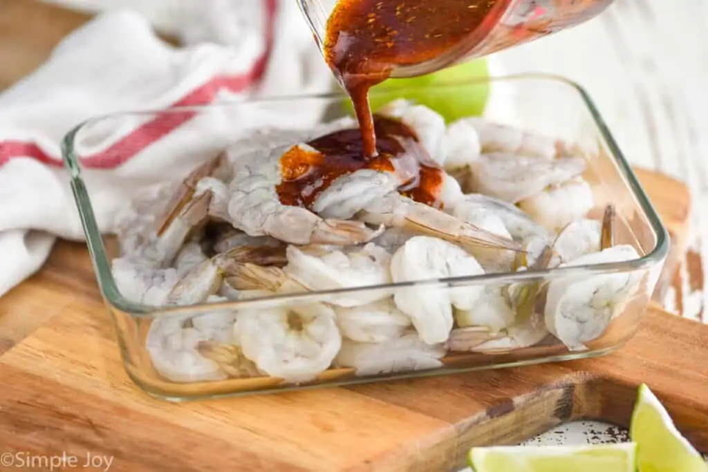 shrimp fajita marinade being poured over raw shrimp in a reusable container