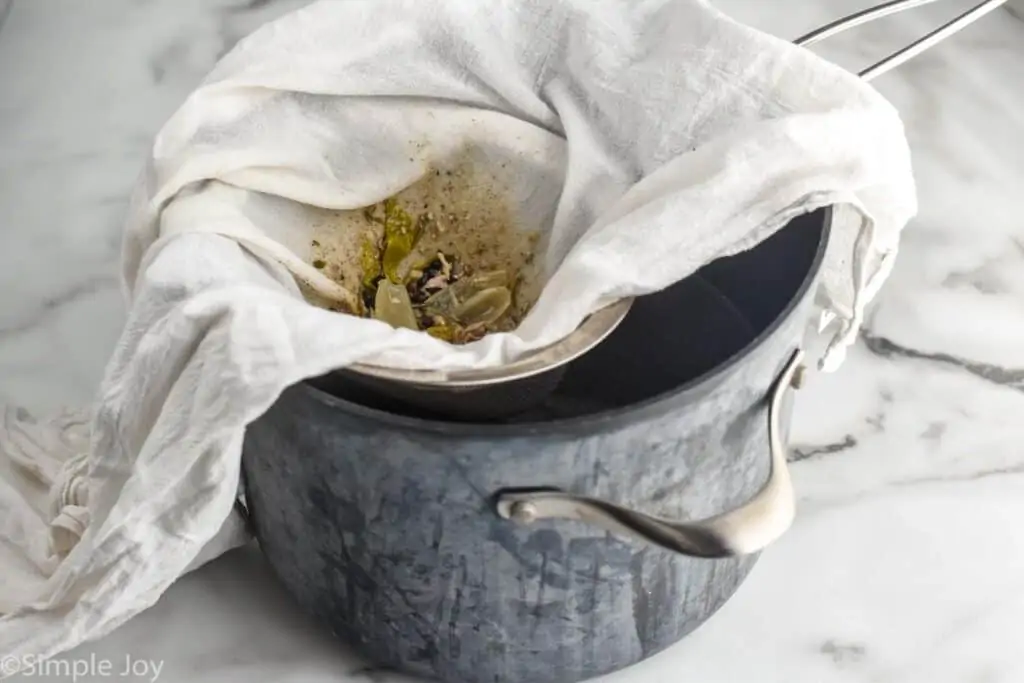 a cheese cloth inside of a mesh strainer over a dutch oven