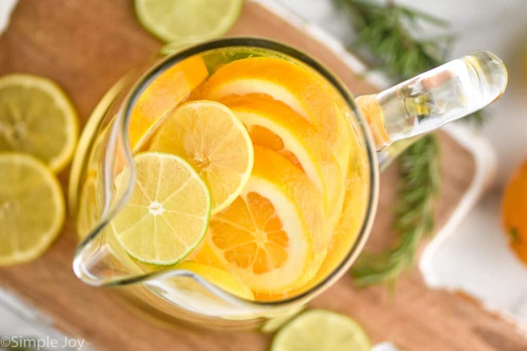 overhead view of a pitcher of white wine sangria with cut up limes, lemons and oranges visible