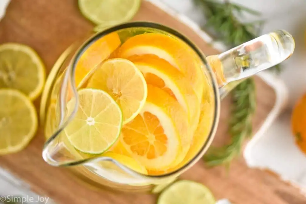 overhead view of a pitcher of white wine sangria with cut up limes, lemons and oranges visible