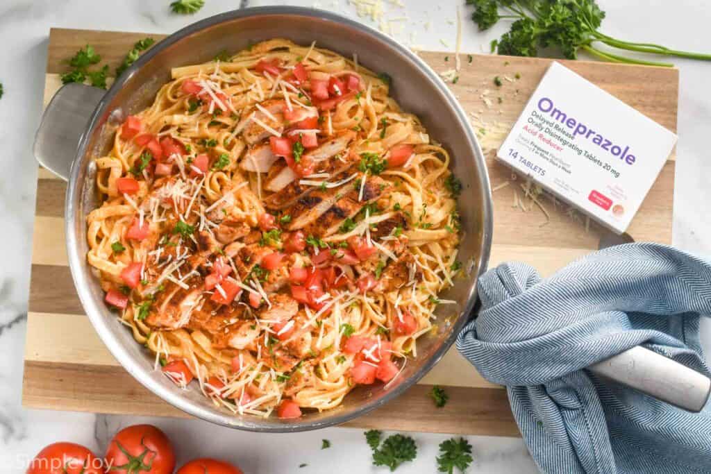 skillet full of Cajun Chicken Pasta Alfredo on a cutting board with a box of omeprazole odd