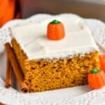 a piece of pumpkin pie cake topped with cream cheese frosting on a plate with candy pumpkins and cinnamon sticks