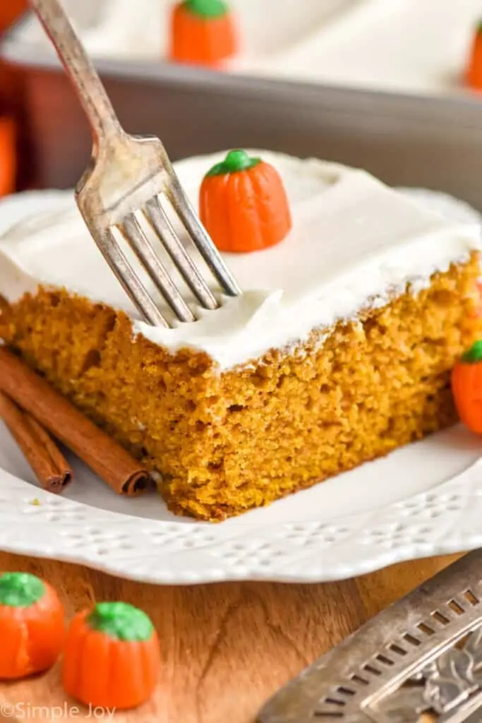 a fork pushing into a piece of pumpkin pie cake topped with cream cheese frosting