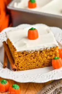 a piece of pumpkin pie cake topped with cream cheese frosting on a plate with candy pumpkins and cinnamon sticks