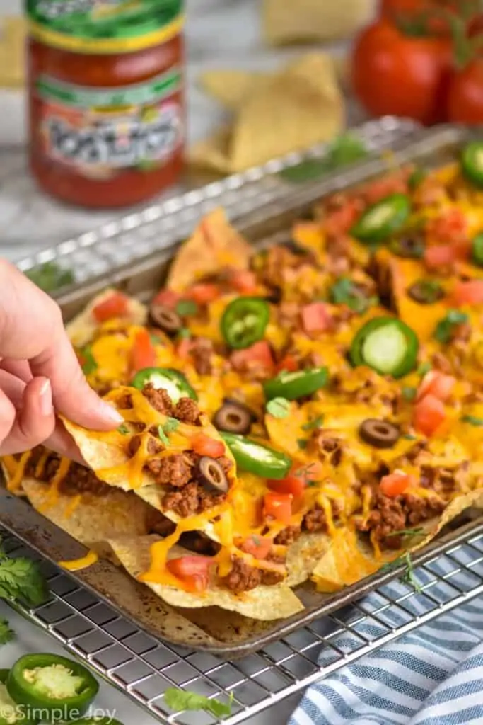 close up look at a hand lifting a chip off a pan of sheet pan nachos