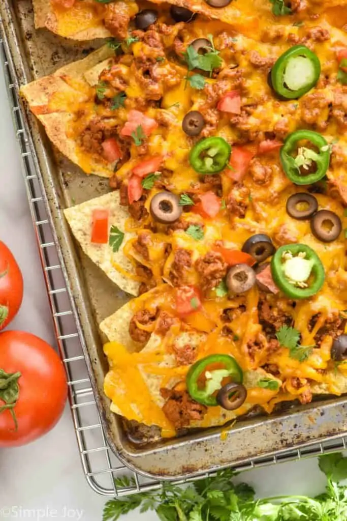 close up overhead view of sheet pan nachos topped with olives, diced tomatoes, and jalapeño slices