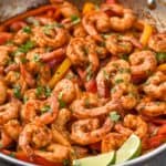 a frying pan full of shrimp fajita recipe topped with fresh cilantro and two lime wedges - 15