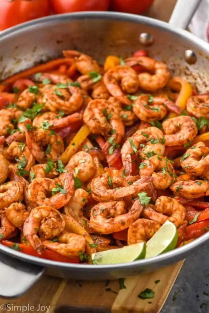 a frying pan full of shrimp fajita recipe topped with fresh cilantro and two lime wedges