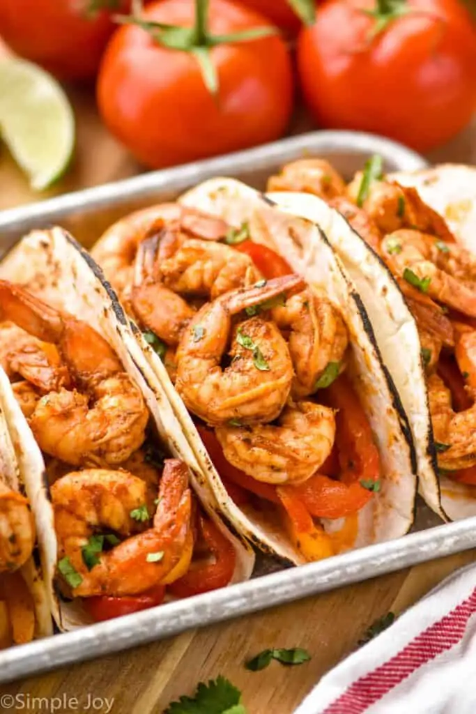 three shrimp fajitas on a metal tray garnished with fresh cilantro